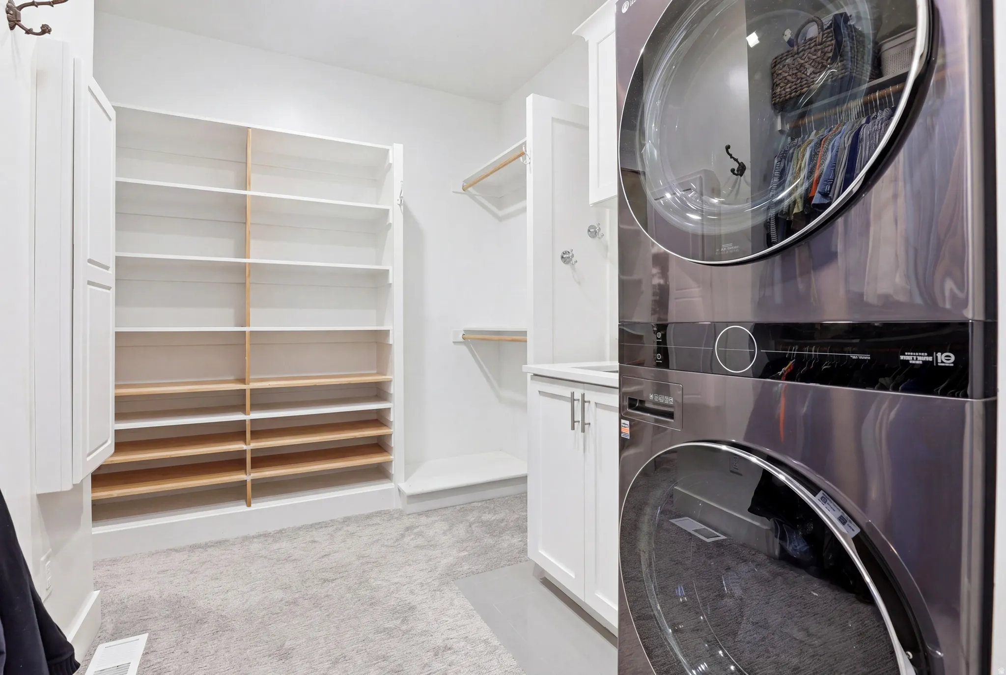 Integrated laundry appliances with custom built-in shelving, white cabinetry, and light-toned carpeting