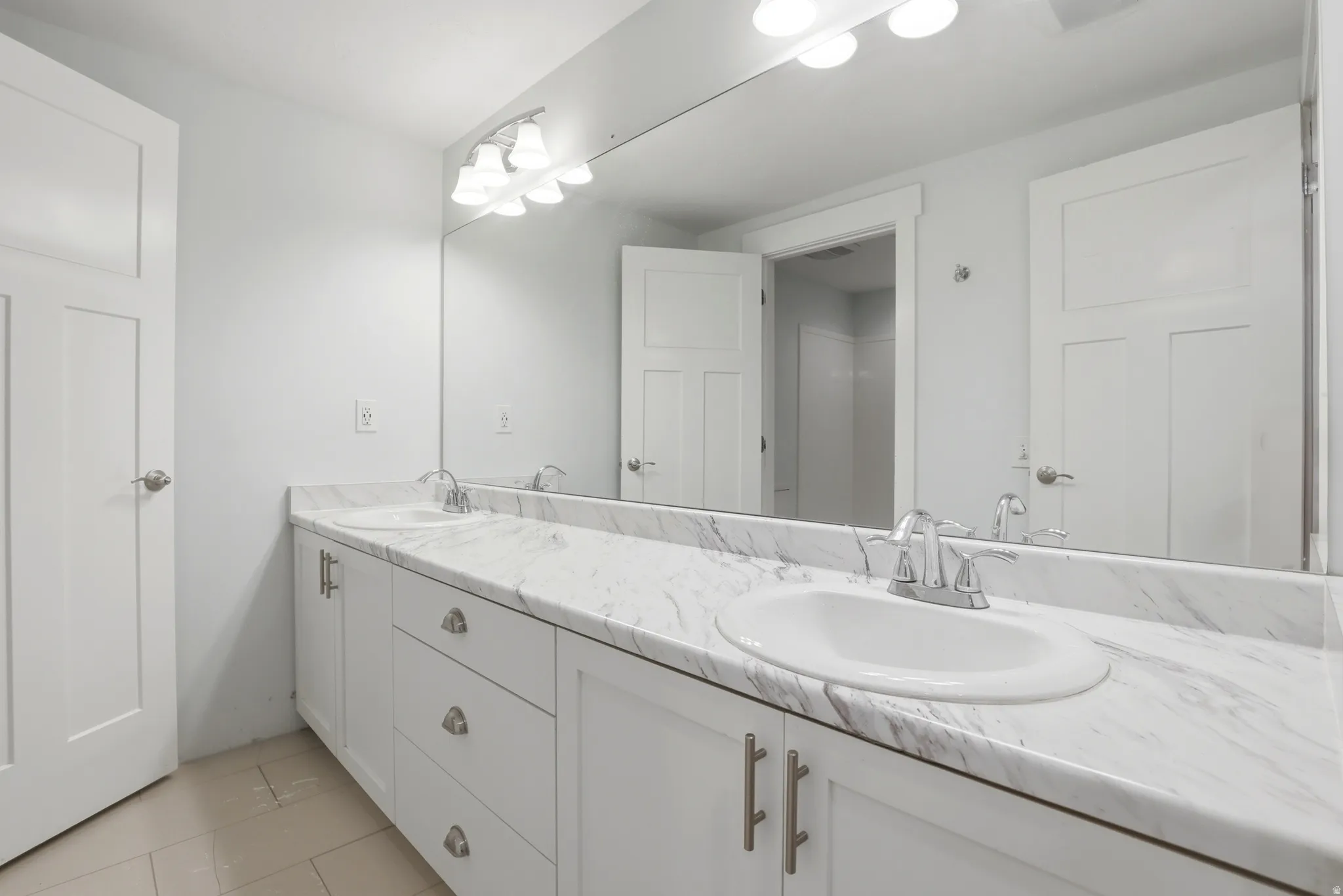 Spacious vanity featuring double undermount sinks, a faux-marble countertop, white cabinetry with silver hardware, and a large wall-mounted mirror