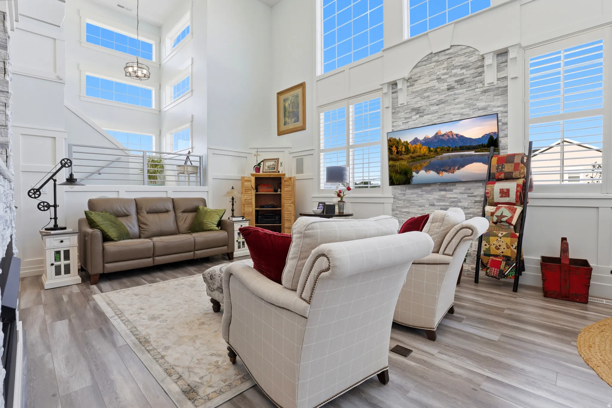 Spacious living area featuring high ceilings, extensive window arrays, light wood-finish flooring, and a decorative accent wall with an integrated television