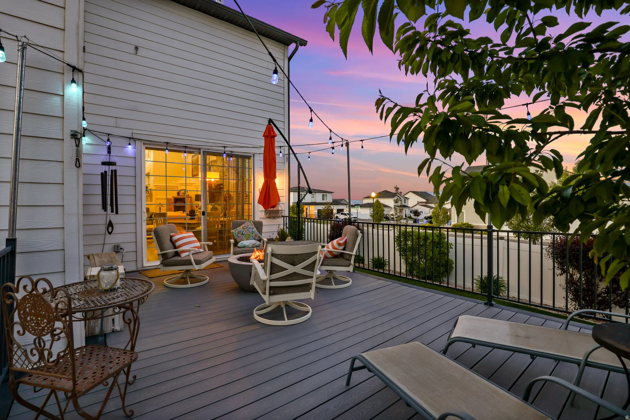 Spacious outdoor deck featuring gray composite decking, black metal railings, string lighting, and sliding glass doors