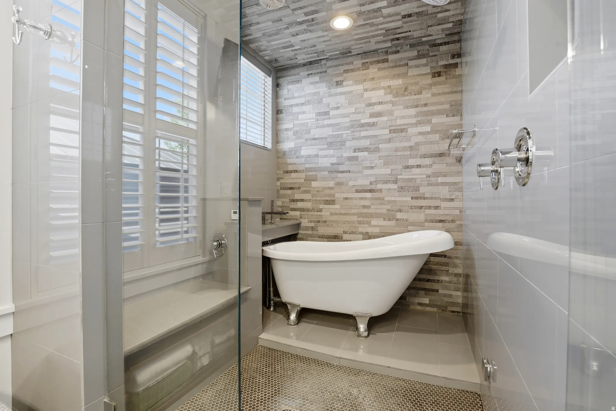 Bathroom featuring a clawfoot tub on a raised platform, glass-enclosed shower with a built-in bench, and a window with plantation shutters