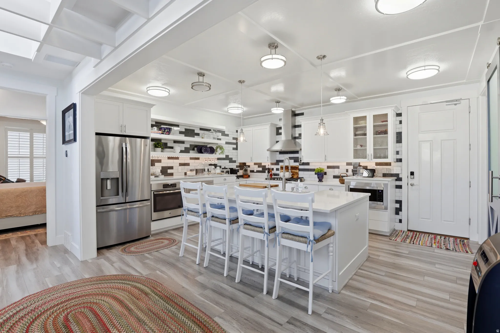 Modern kitchen featuring a central island with seating, stainless steel appliances, white cabinetry, and a distinctive multi-toned tile backsplash