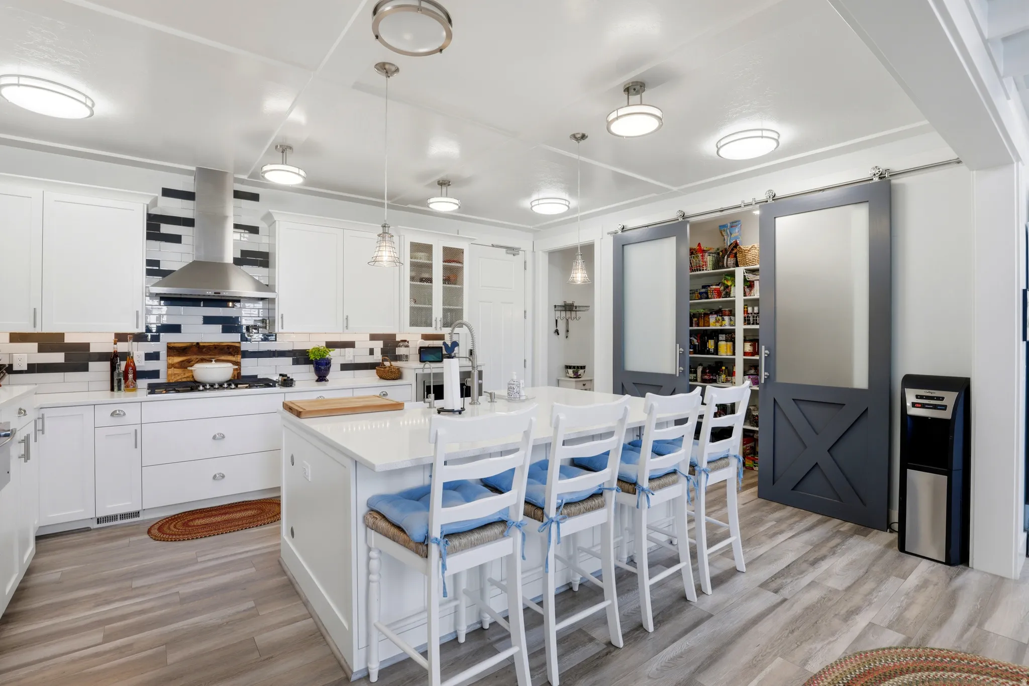 Bright kitchen featuring an expansive center island with seating, white shaker cabinetry, stainless steel range hood, and wood-finish flooring