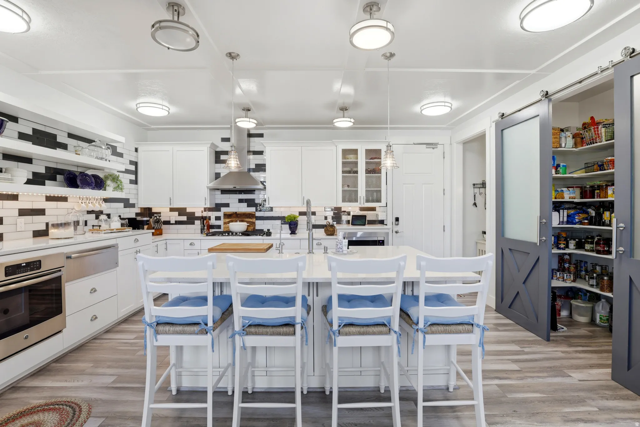 Spacious kitchen featuring an expansive central island, white cabinetry, integrated stainless steel appliances, and wood-finish flooring