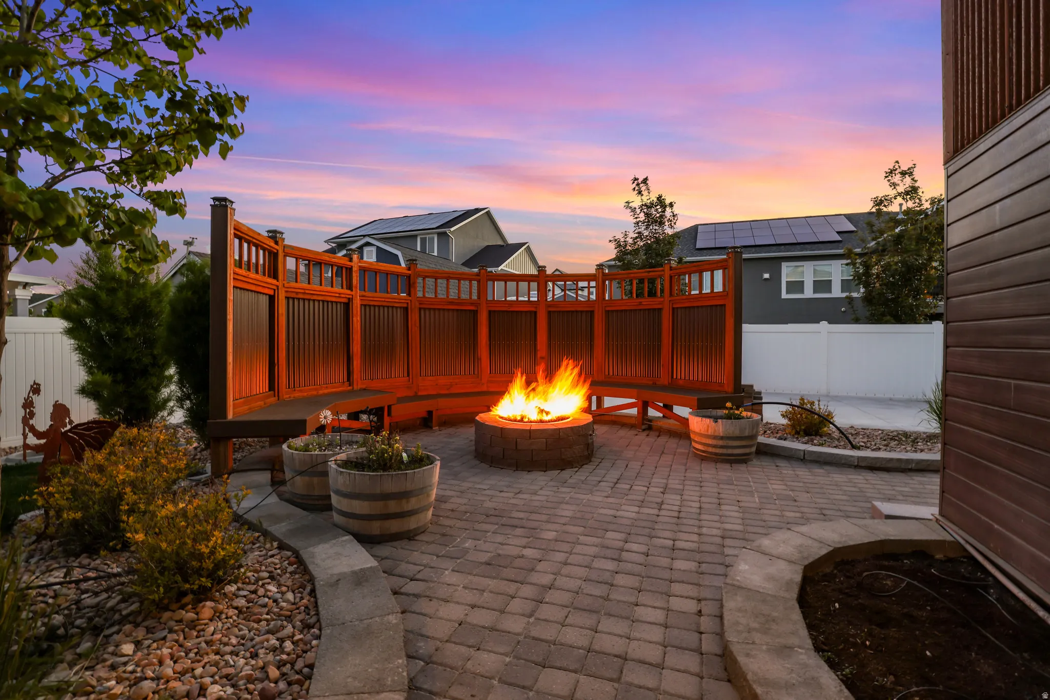 Paver patio featuring a built-in fire pit, curved wooden privacy wall, integrated bench seating, and landscaped borders