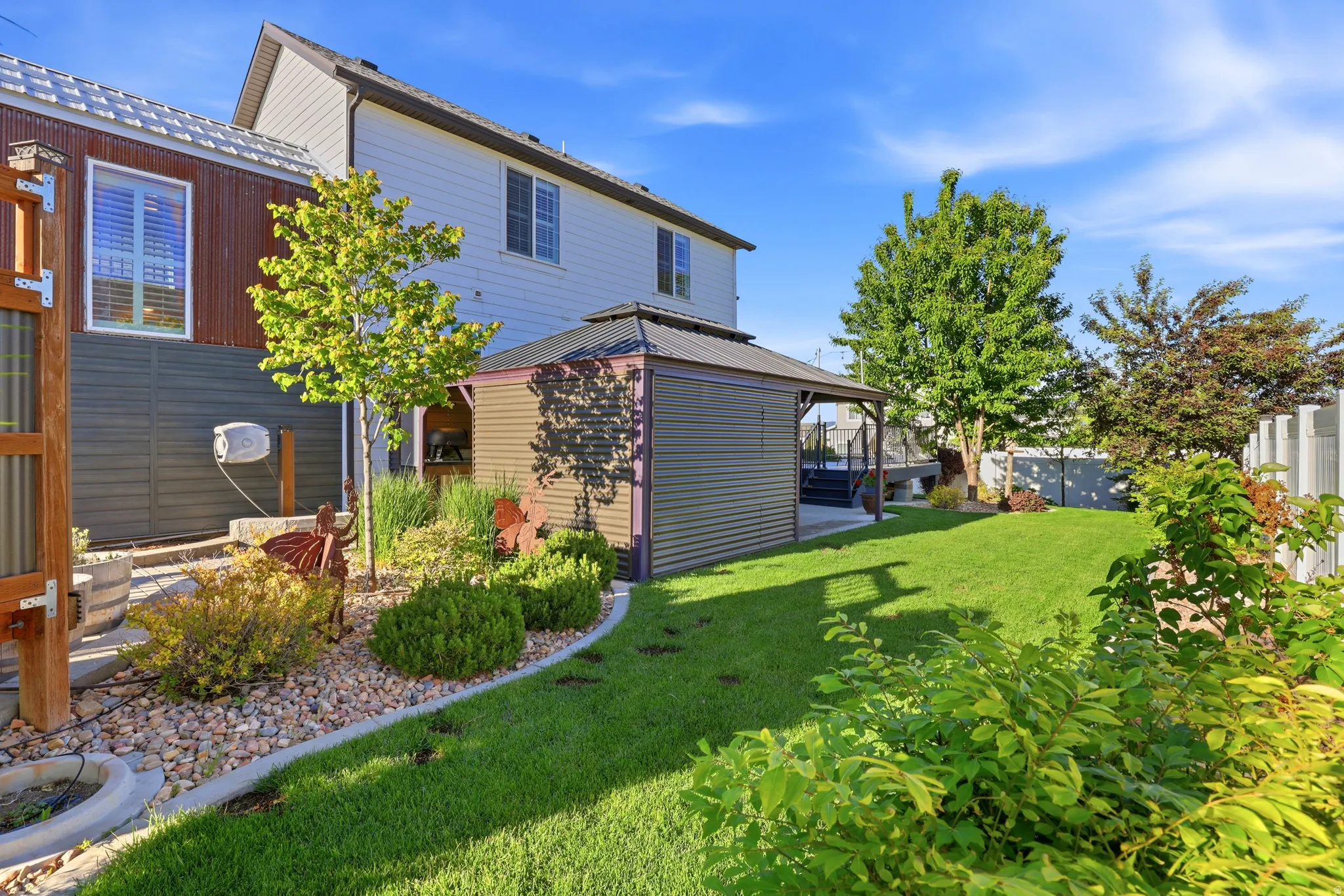 Expansive backyard featuring a manicured lawn, a gravel pathway with garden beds, a covered gazebo, and mature trees