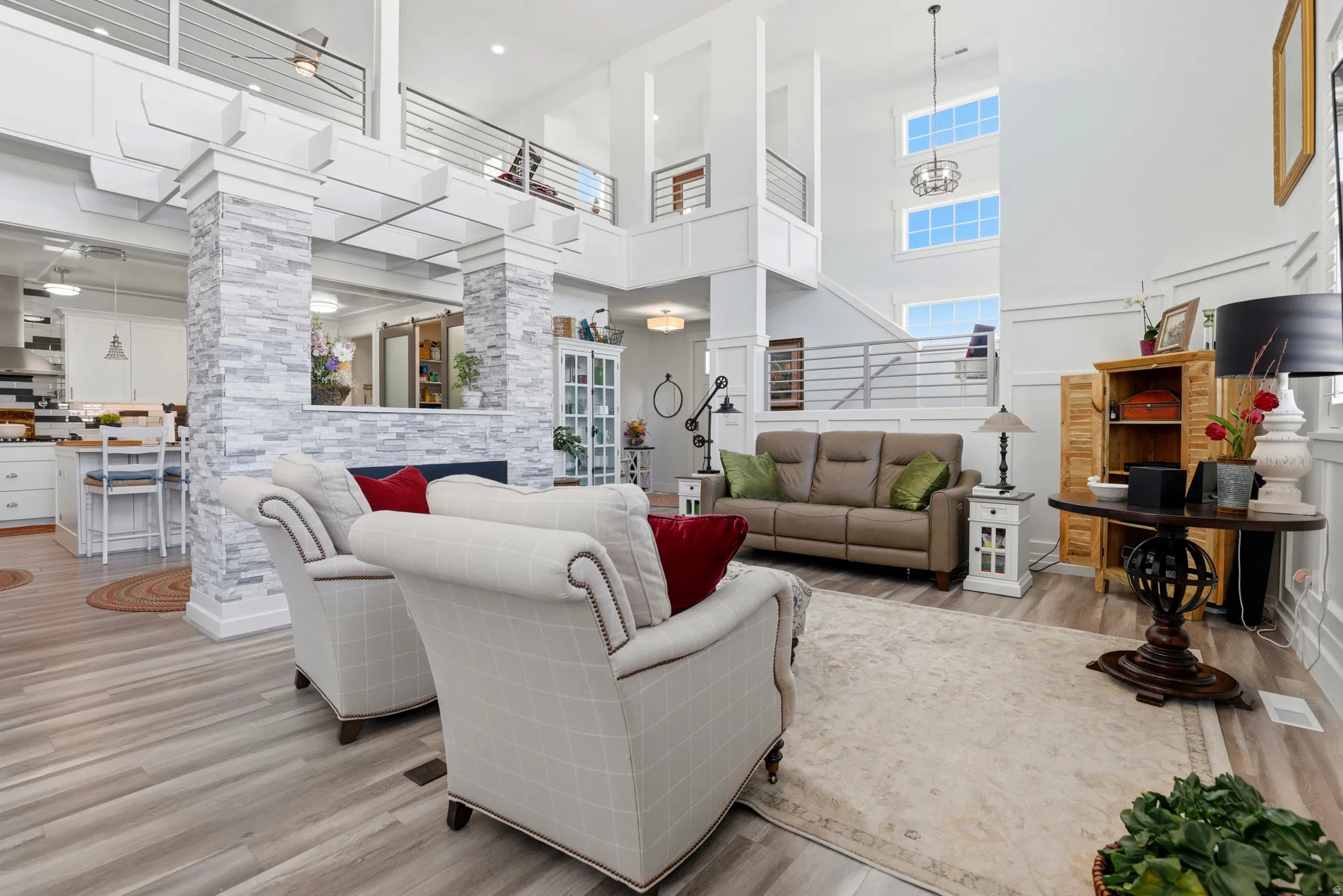 Two-story living area featuring a stacked stone fireplace, wood-finish flooring, white wainscoting, and large upper-level windows