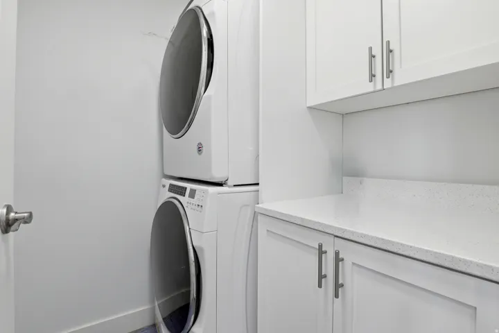 Laundry area featuring stackable appliances, white cabinetry, a light-toned countertop, and brushed nickel hardware