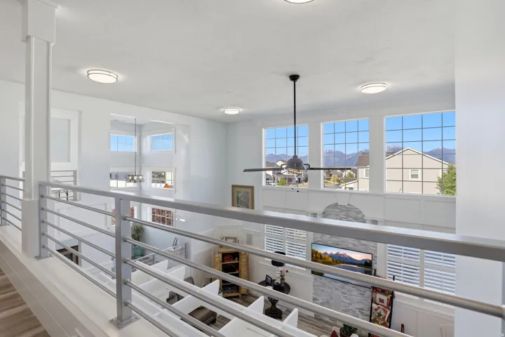 Open loft overlooking a living area with high ceilings, large windows, and a ceiling fan