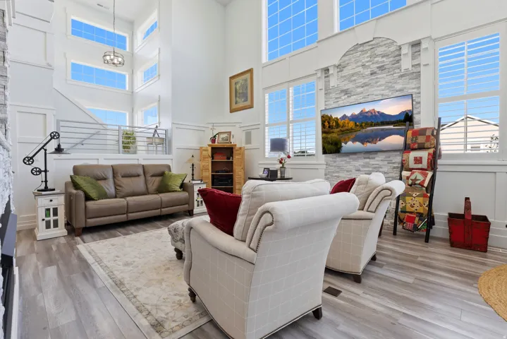 Spacious living area featuring high ceilings, extensive window arrays, light wood-finish flooring, and a decorative accent wall with an integrated television