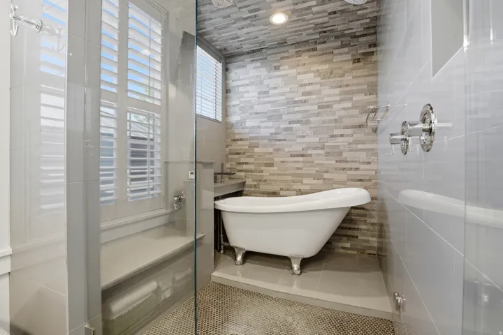 Bathroom featuring a clawfoot tub on a raised platform, glass-enclosed shower with a built-in bench, and a window with plantation shutters
