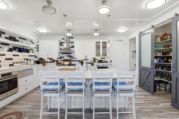 Spacious kitchen featuring an expansive central island, white cabinetry, integrated stainless steel appliances, and wood-finish flooring