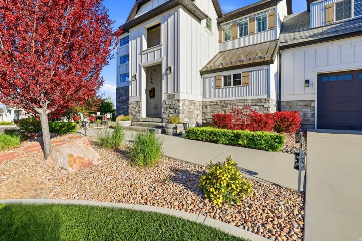 Modern farmhouse exterior with vertical white siding, stone accents, a dark garage door, a corrugated metal awning, and decorative wooden shutters