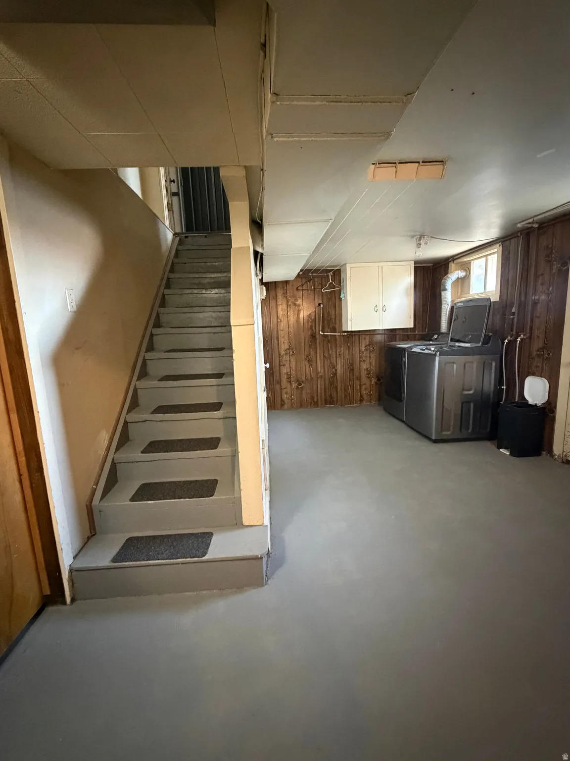 Spacious lower level featuring a painted concrete floor, wood-paneled walls, and a utility area with built-in cabinetry