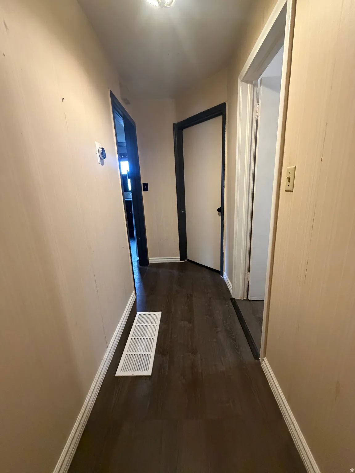 Hallway featuring dark wood-finish flooring, light tan walls, white baseboards, and white ceiling light fixture