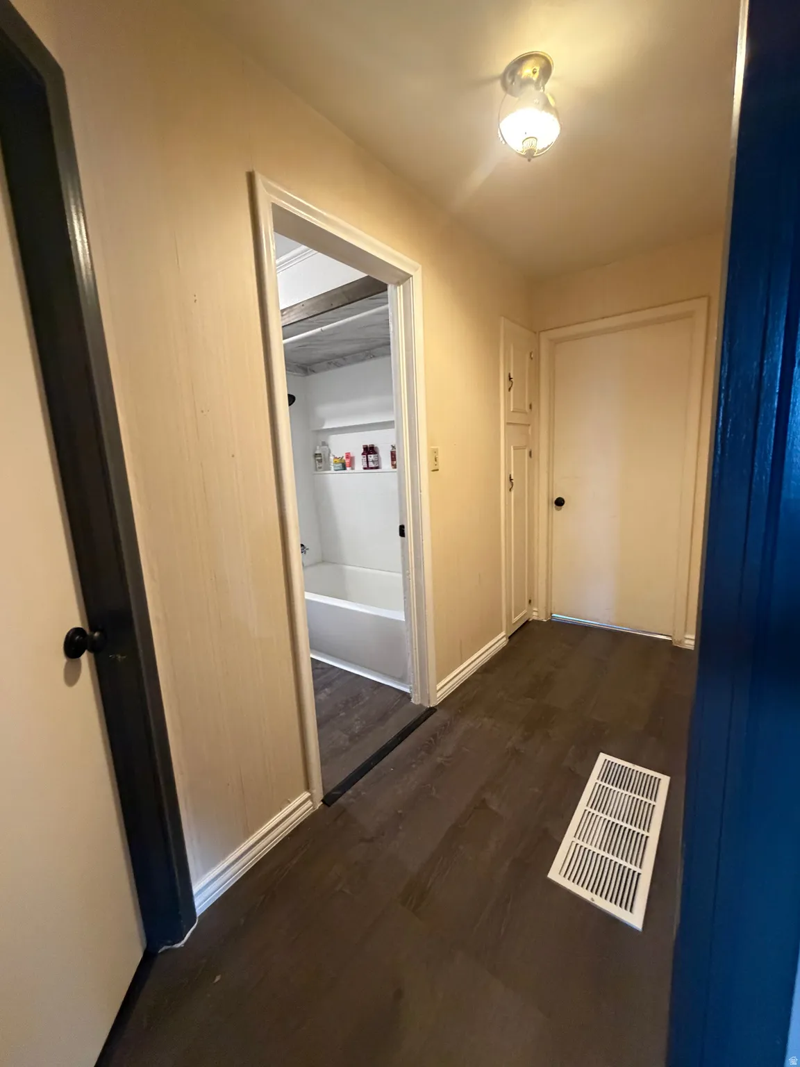 Hallway featuring dark wood-finish flooring, light wall paint, and white trim