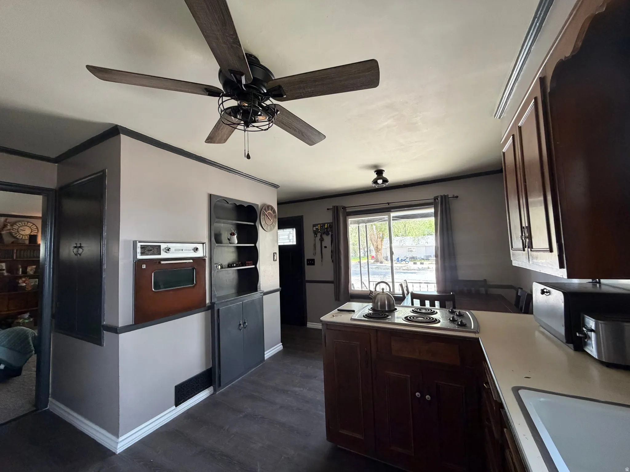 Kitchen featuring a ceiling fan, built-in oven, built-in shelving, wood-finish flooring, and slider door