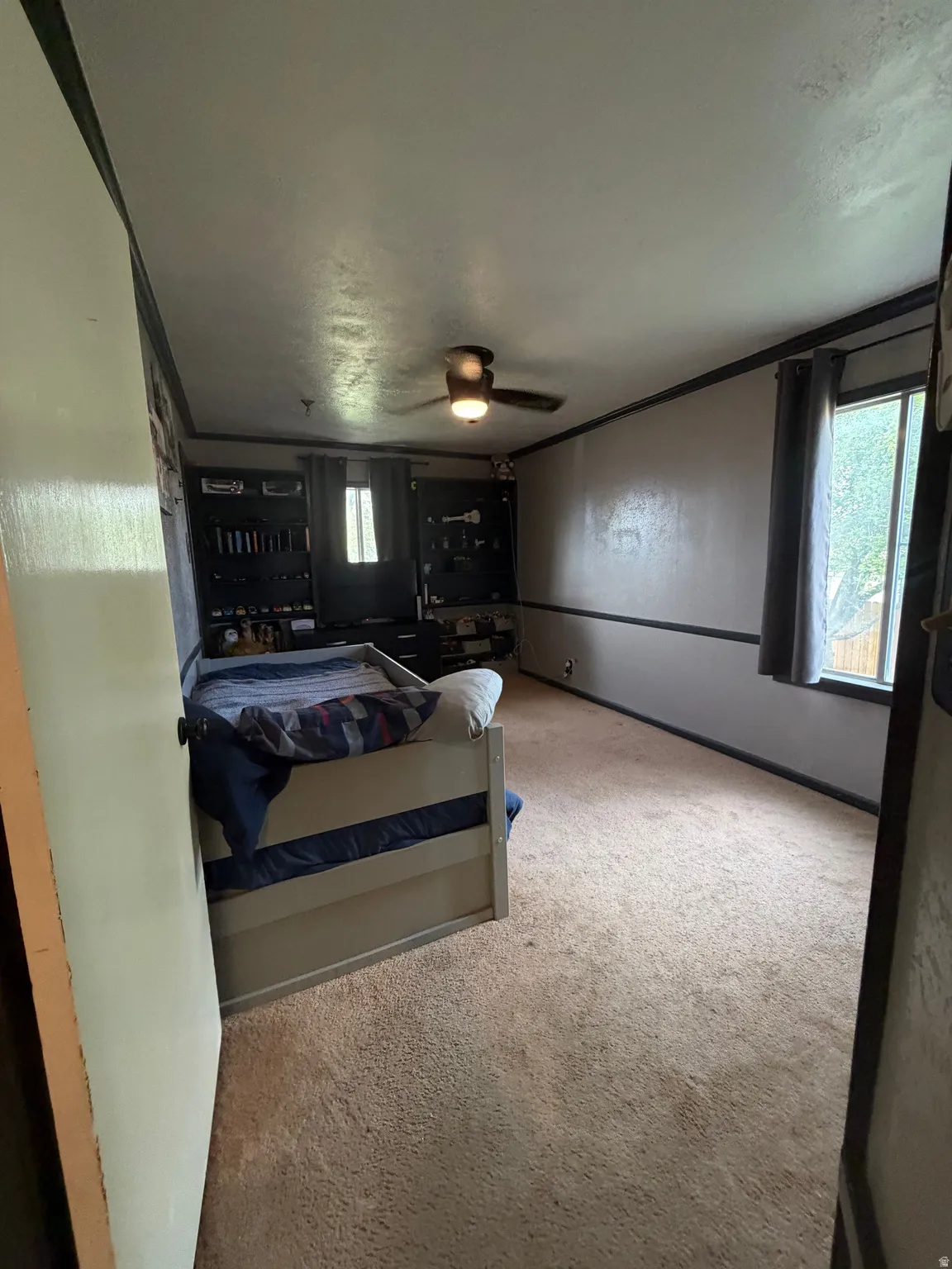 Carpeted room featuring a ceiling fan, baseboard trim, and window with dark drapes