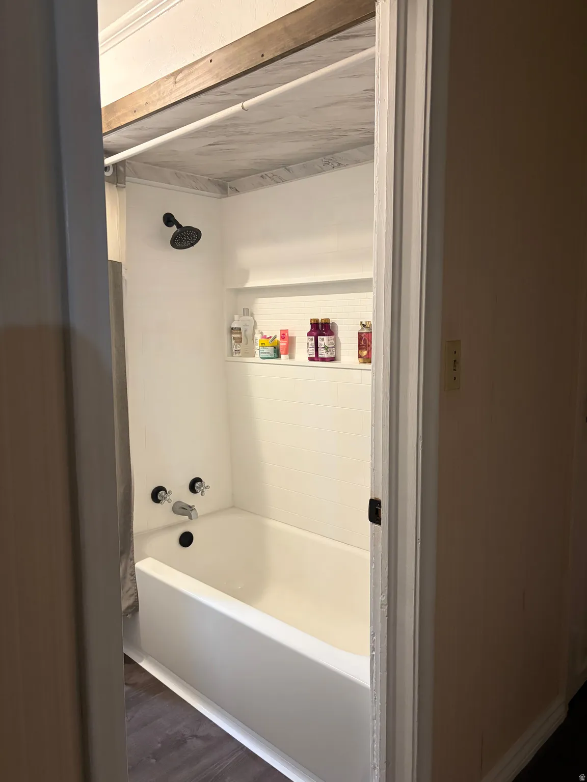 Bathtub and shower combination featuring a white surround, integrated shelving, and a matte black showerhead