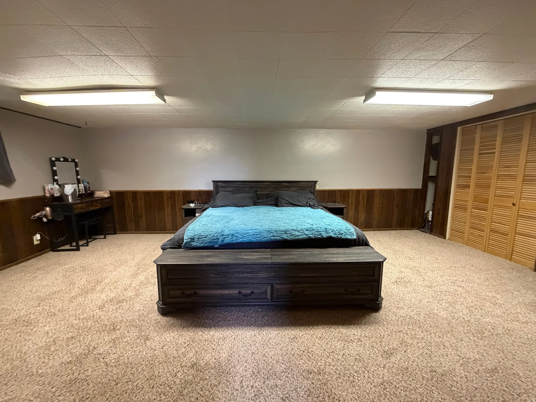 Carpeted room featuring wood-panel wainscoting and bi-fold louvered closet doors