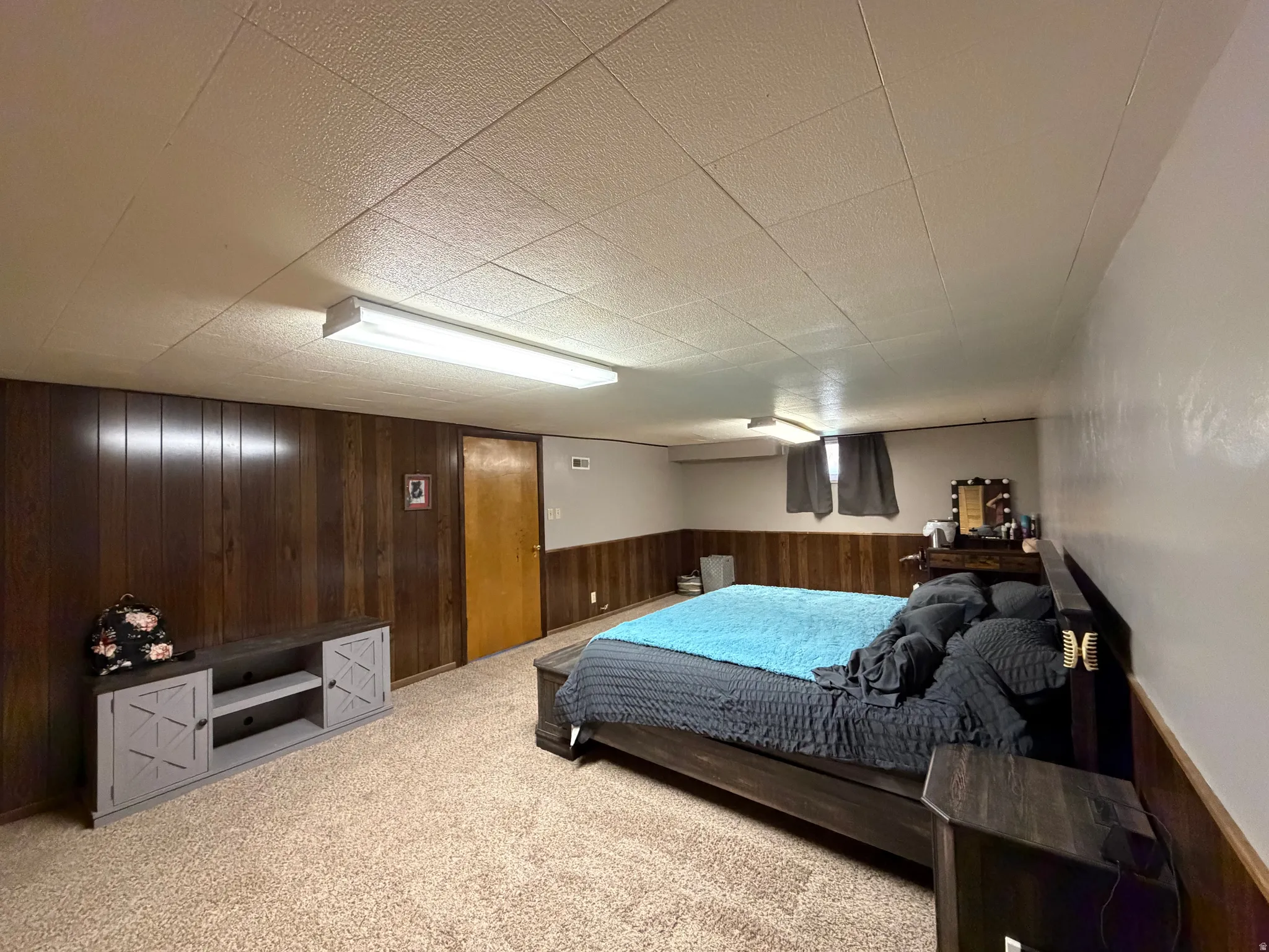 Carpeted room featuring wood-panel wainscoting and a drop-panel ceiling