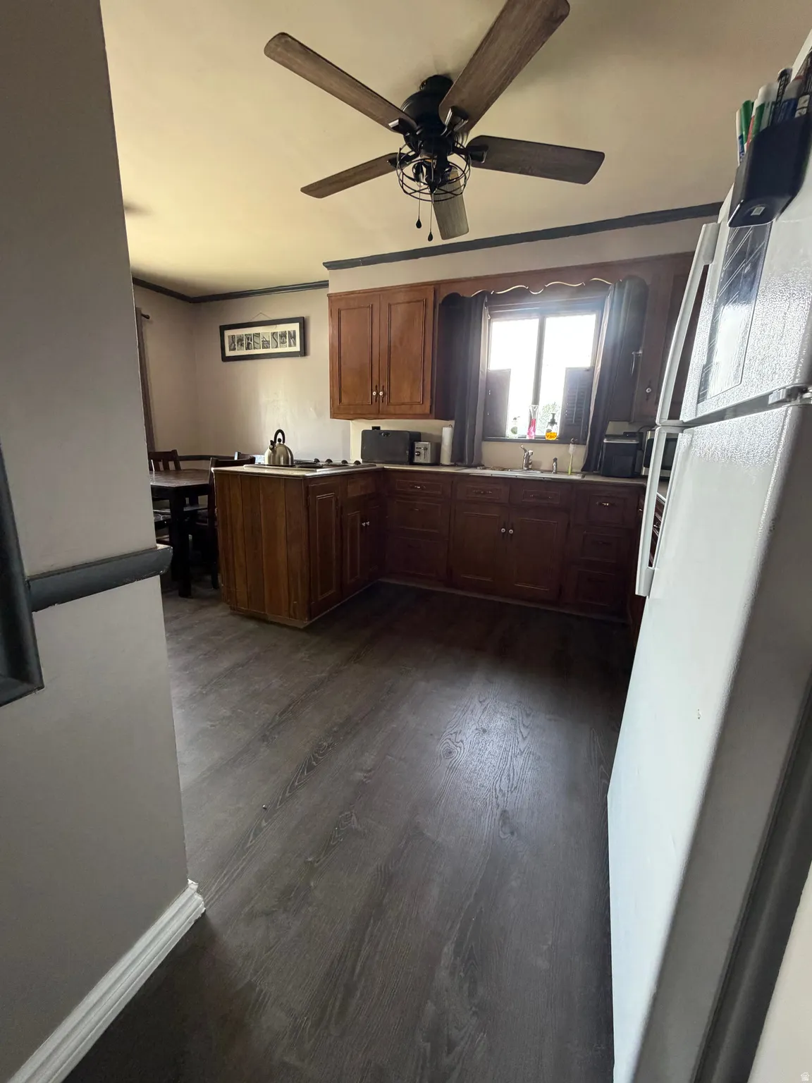 Kitchen area featuring wood-finish flooring, wood cabinetry, a window above the sink, and a ceiling fan