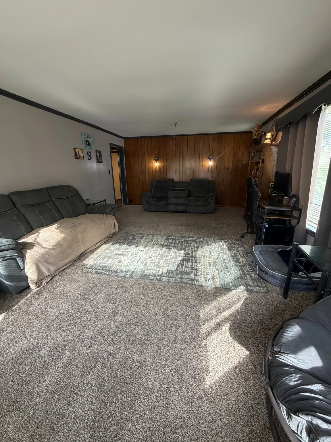 Spacious room featuring neutral carpeting and a wood-paneled accent wall with sconce lighting