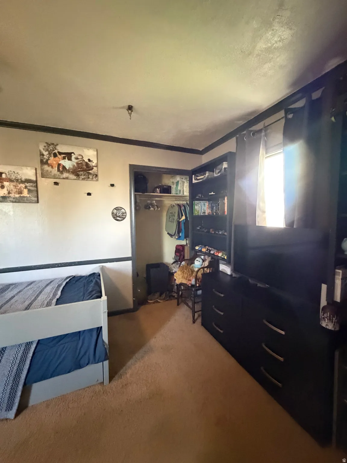 Carpeted room featuring a built-in closet with shelving, a window with dark curtains, and crown molding