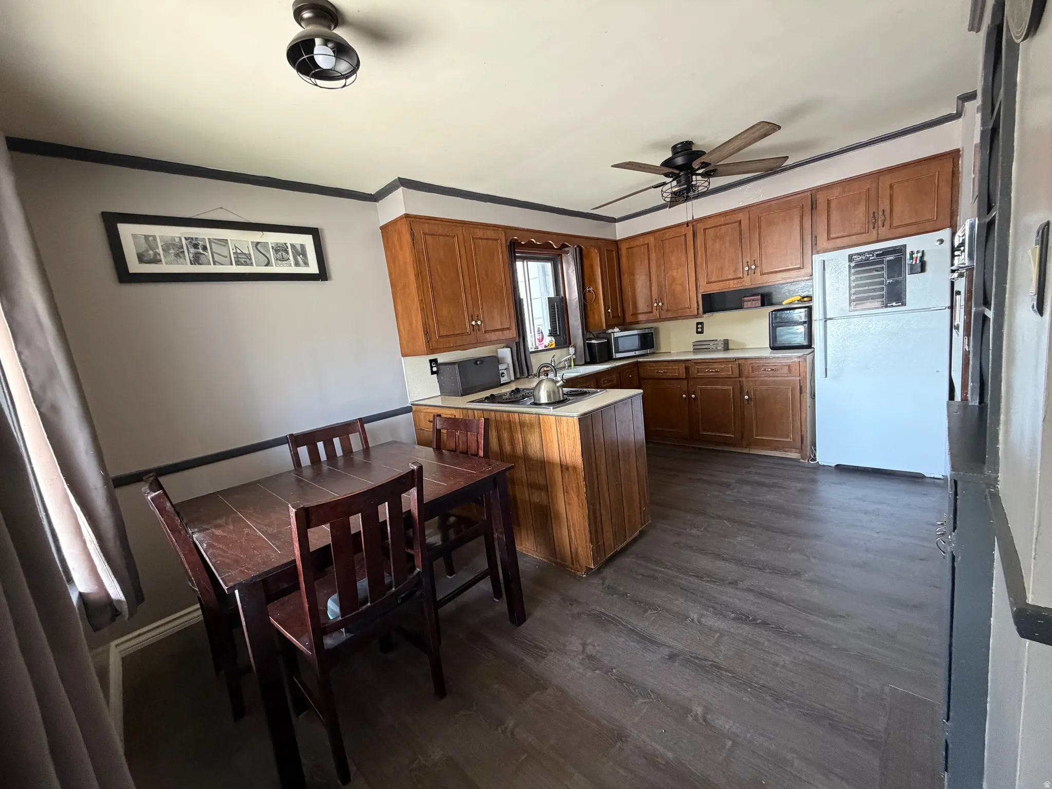 Kitchen area featuring extensive wood cabinetry, dark wood-finish flooring, a ceiling fan with integrated lighting, and a built-in kitchen island