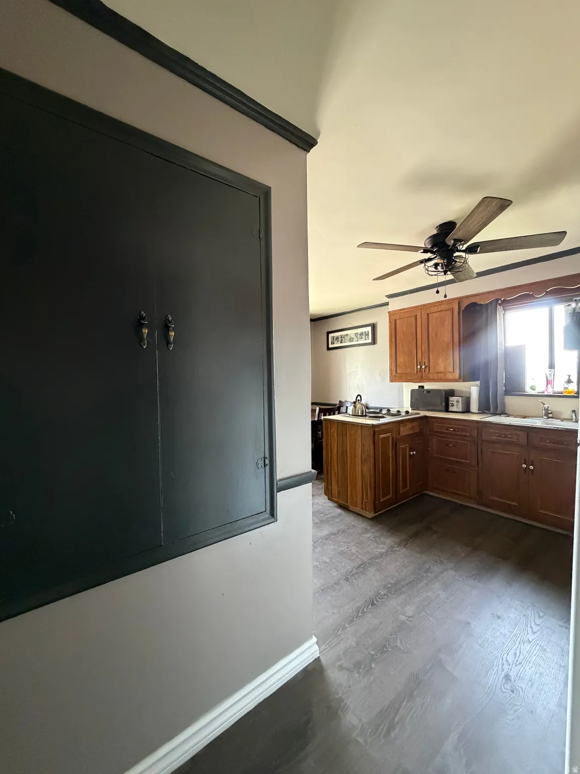 Kitchen featuring wood-finish flooring, wood cabinetry, a ceiling fan with light fixture, and a window with a valance