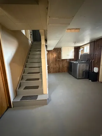 Spacious lower level featuring a painted concrete floor, wood-paneled walls, and a utility area with built-in cabinetry