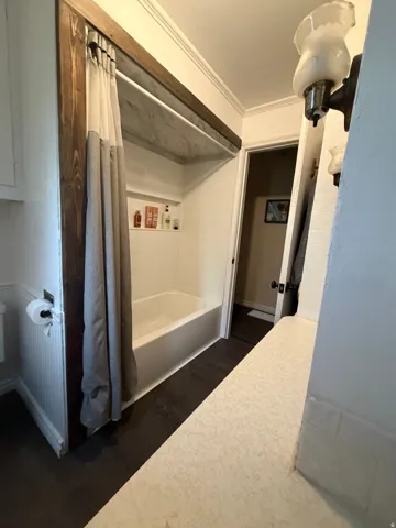 Bathroom featuring a white bathtub, built-in shower niche, dark wood-finish flooring, and a textured countertop