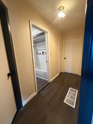 Hallway featuring dark wood-finish flooring, light wall paint, and white trim
