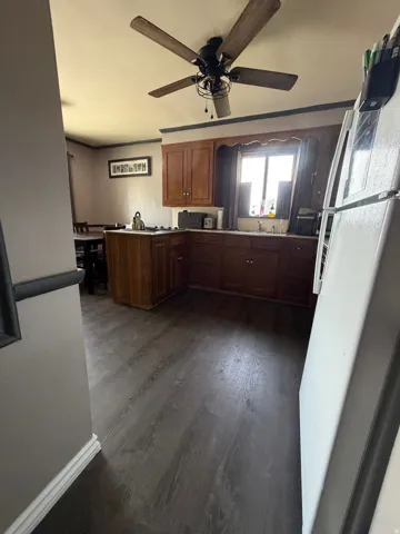 Kitchen area featuring wood-finish flooring, wood cabinetry, a window above the sink, and a ceiling fan