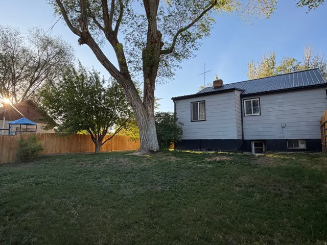 Expansive rear yard featuring mature trees, a privacy fence, and a light-colored exterior with a dark metal roof