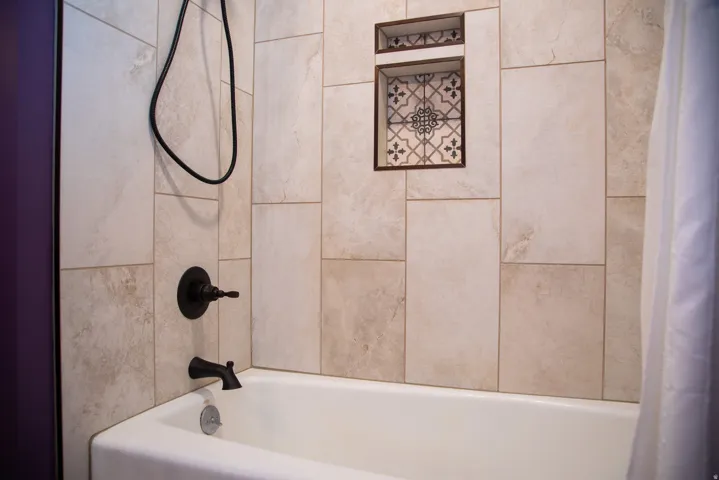 Bathtub with light-toned rectangular tile surround.  Laundry chute in this bathroom leading directly to laundry room.