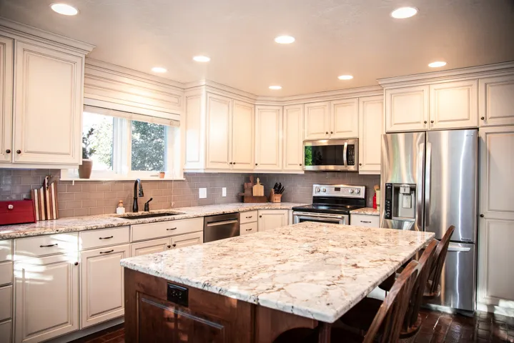 Kitchen featuring white cabinetry, stainless steel appliances, a tile backsplash, light-toned countertops, and a central island with an extended counter