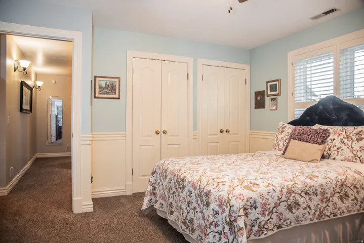 Bedroom featuring twin bi-fold closet doors, light blue walls with cream wainscoting, and plantation shutters