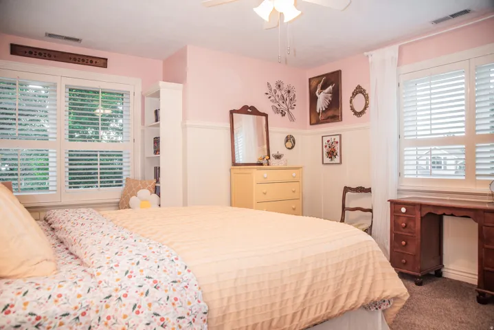 Bedroom featuring two windows with white plantation shutters, white built-in shelving and a large window seat.