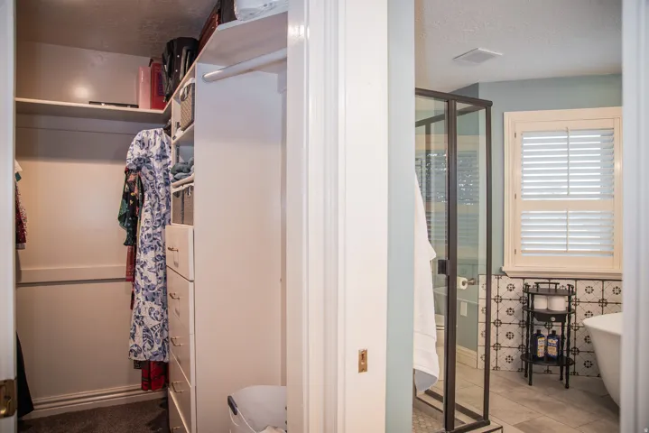 Primary bedroom closet with built-in shelving, integrated drawers, and hanging rods. Partial view into primary bathroom.