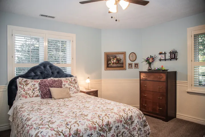 Bedroom featuring two windows with white plantation shutters, two-tone wall treatment with wainscoting, and carpet