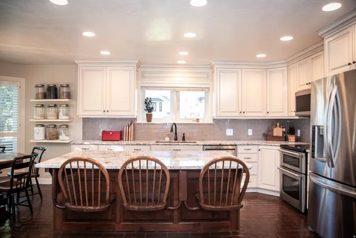 Kitchen featuring white cabinetry, granite countertops, tile backsplash, stainless steel appliances, and a central island with integrated seating