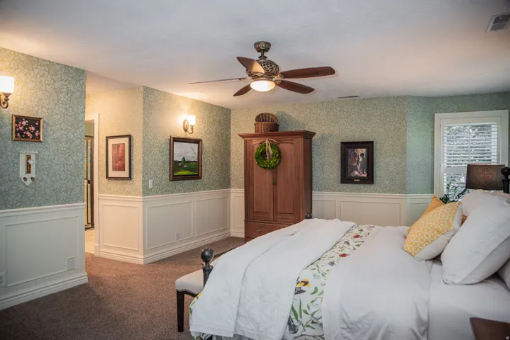 Primary bedroom featuring patterned wallpaper, wainscoting, and carpet.