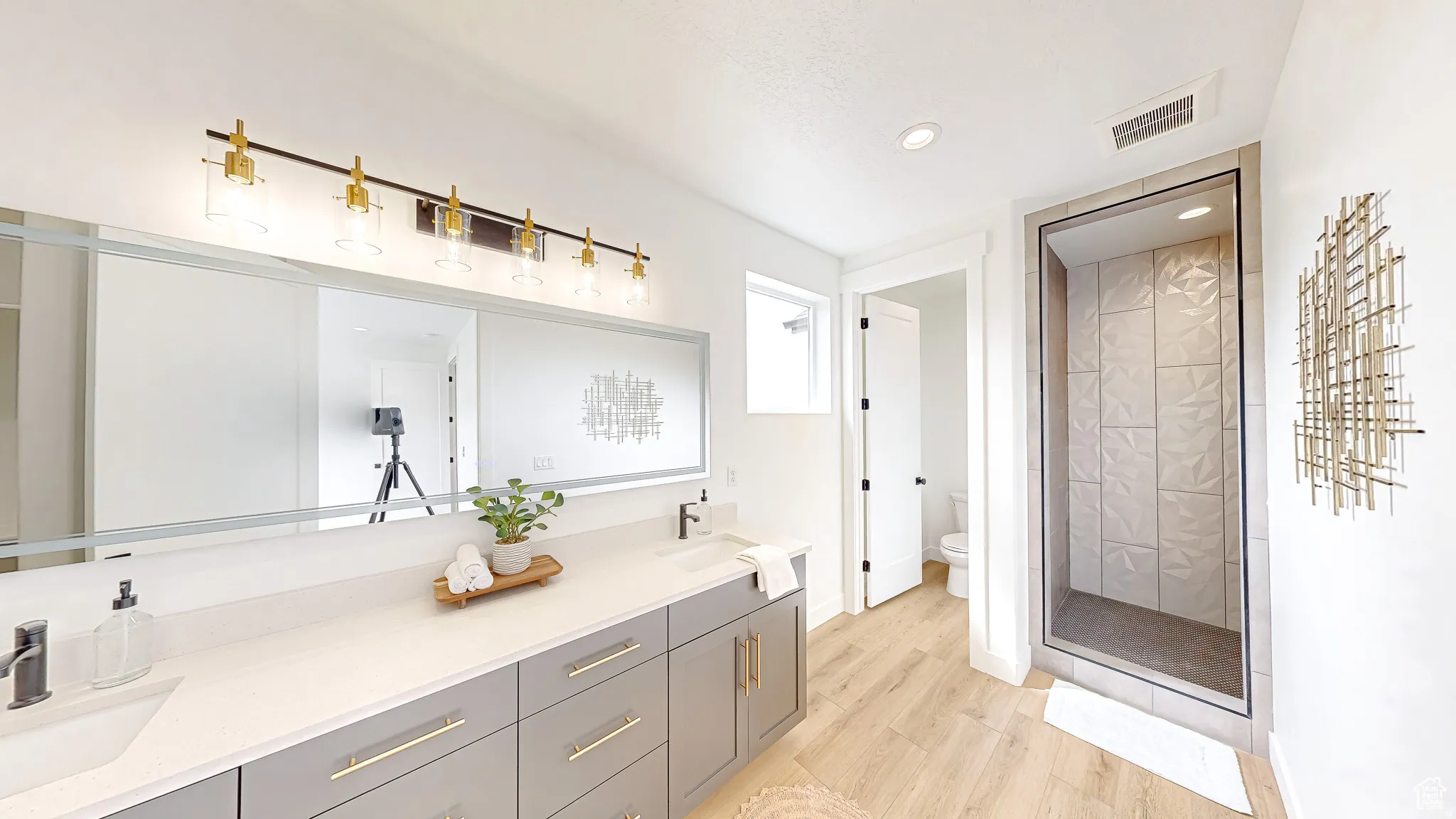 Bathroom with an extended dual-sink vanity featuring a light countertop and gray cabinetry with gold-tone hardware