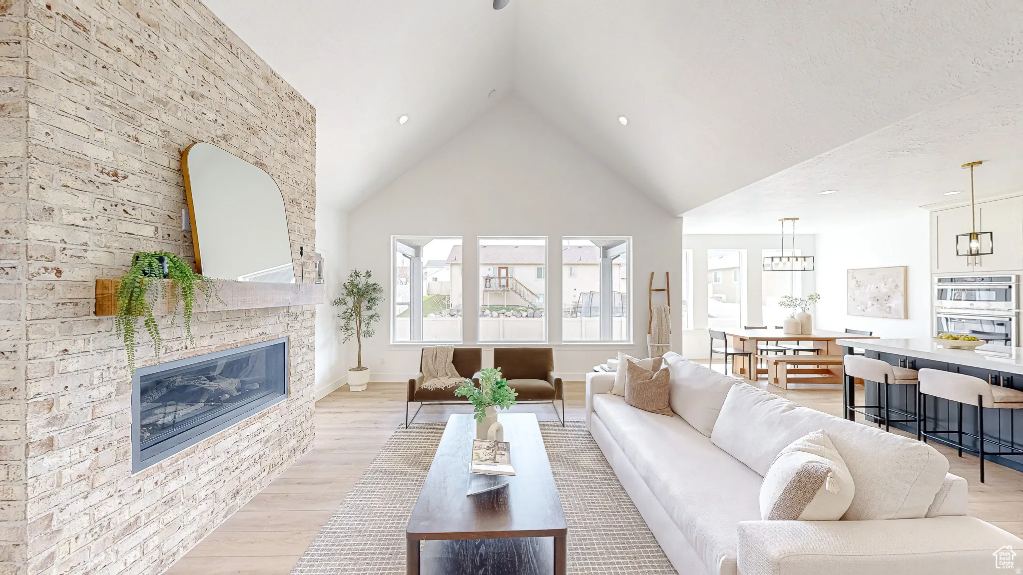 Vaulted ceiling living space featuring a linear fireplace with a distressed brick surround and a wood mantel