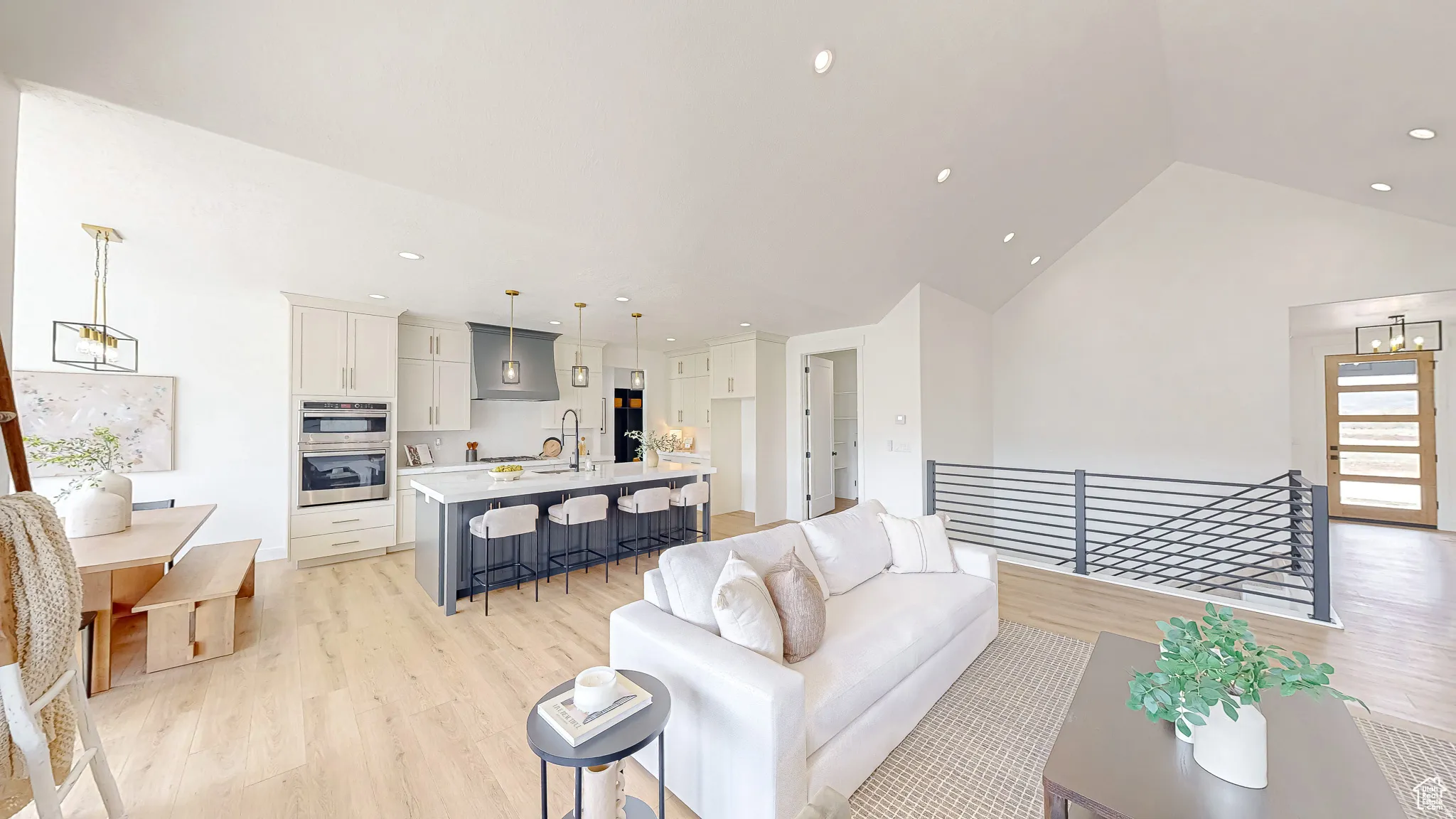 Open-concept interior featuring light wood-finish flooring, a vaulted ceiling, and a modern kitchen with a large island