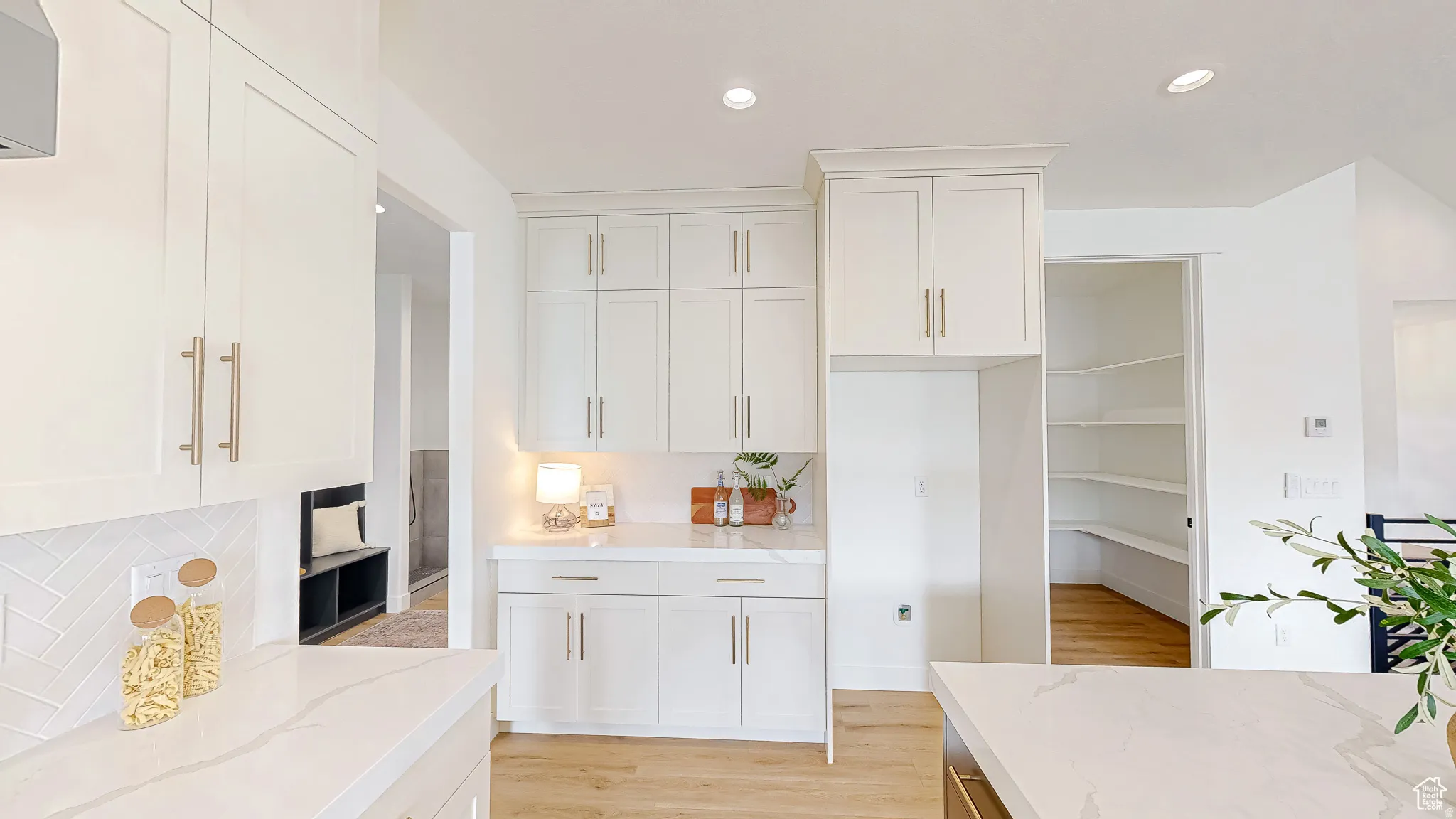 Modern kitchen with white cabinetry, quartz countertops, a herringbone tile backsplash, and a corner pantry with built-in shelving
