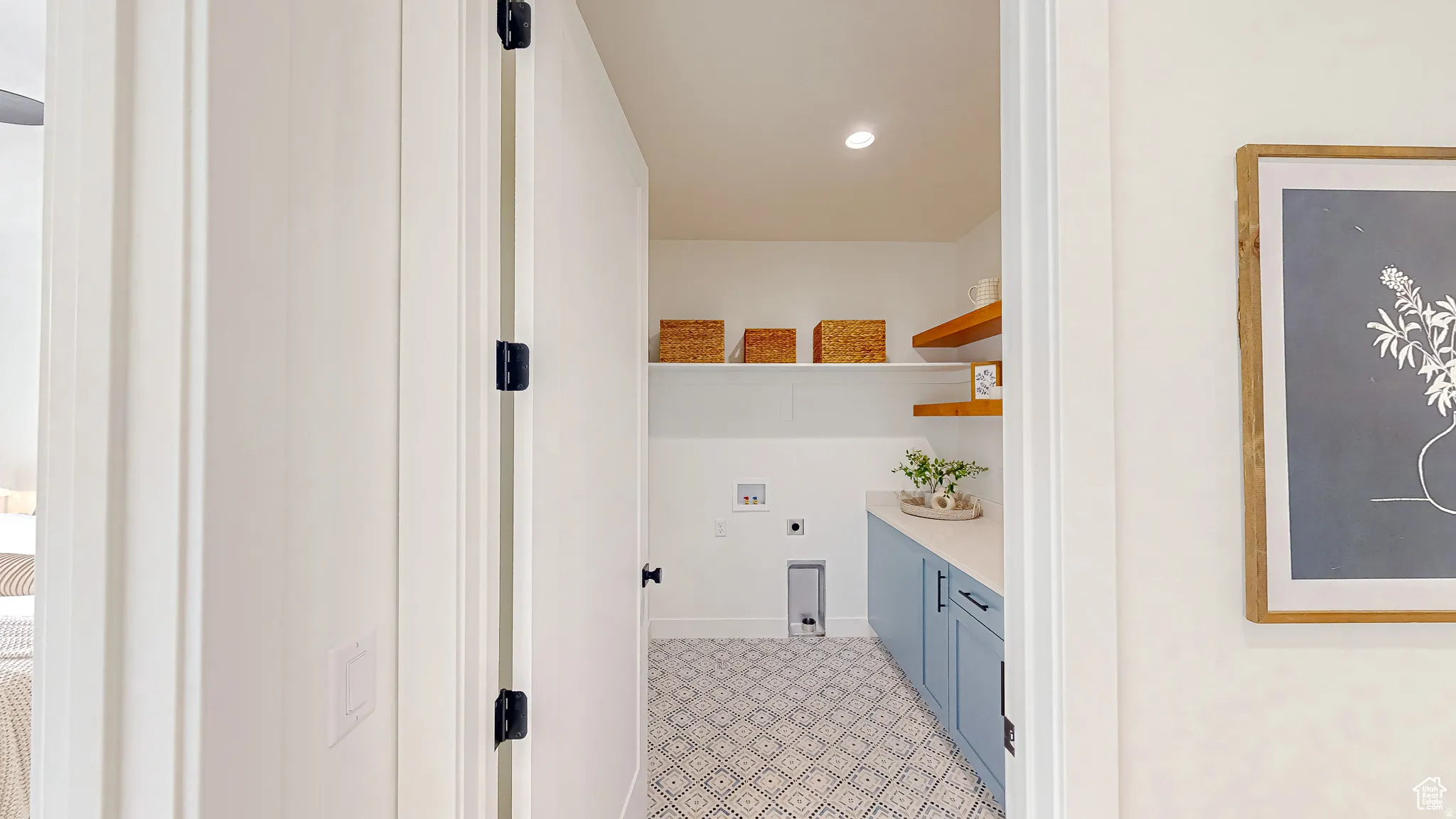 Dedicated laundry room featuring patterned floor tiles, light blue cabinetry with dark hardware, a white countertop, and two levels of open shelving