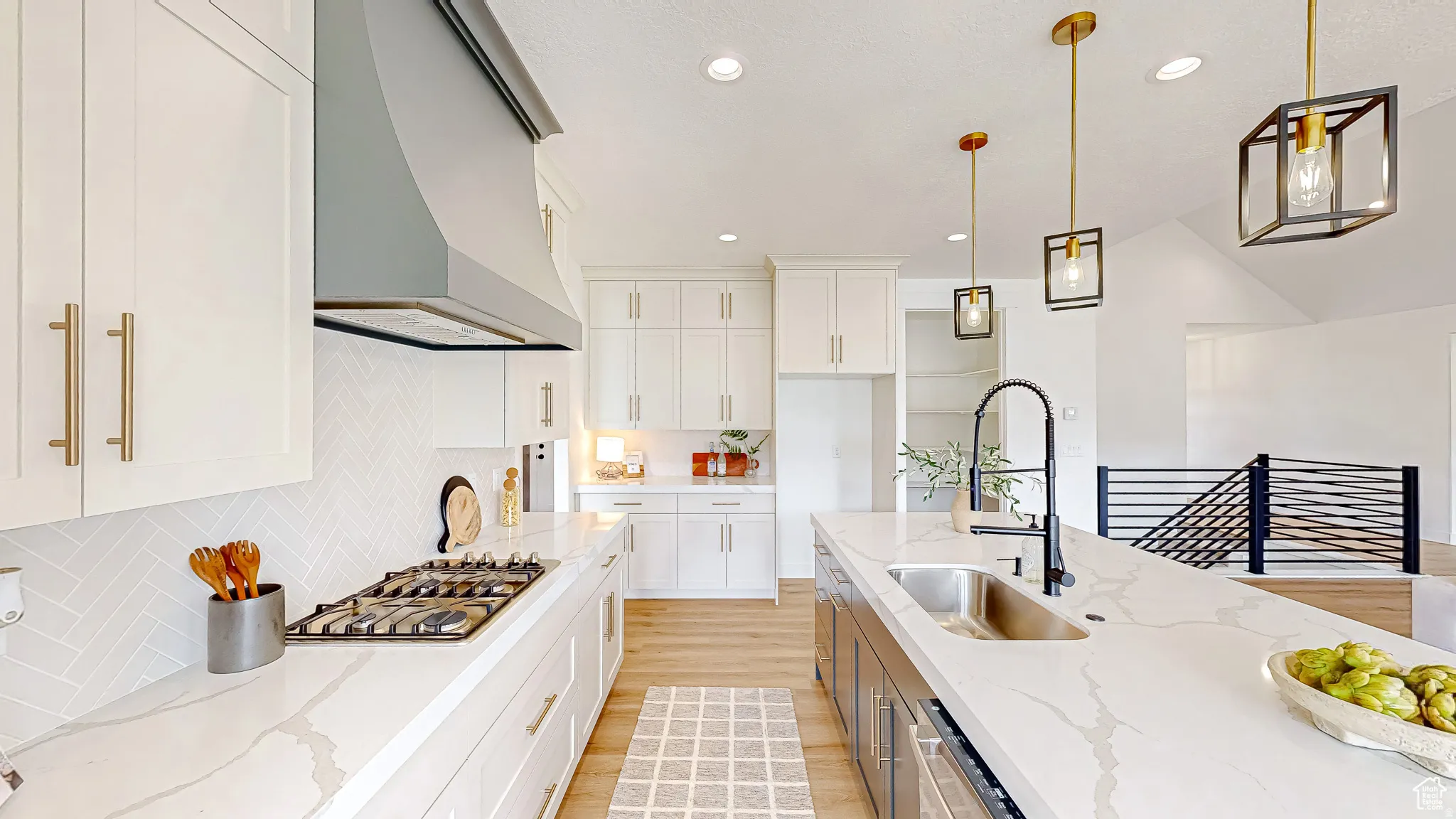 Contemporary kitchen featuring an expansive island with an undermount sink and matte black faucet, custom white cabinetry, quartz countertops, a herringbone tile backsplash, and wood-finish flooring
