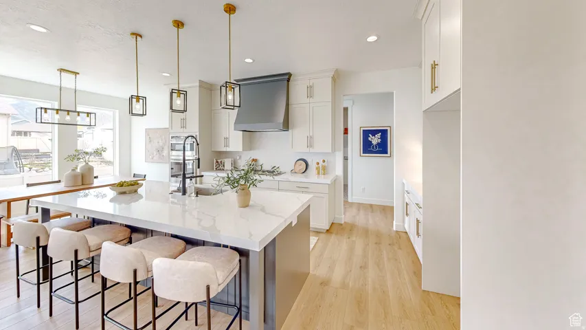 Spacious kitchen featuring an expansive island with a marble-look countertop, white shaker cabinetry, gold-tone hardware, wood-finish flooring, and contemporary pendant lighting